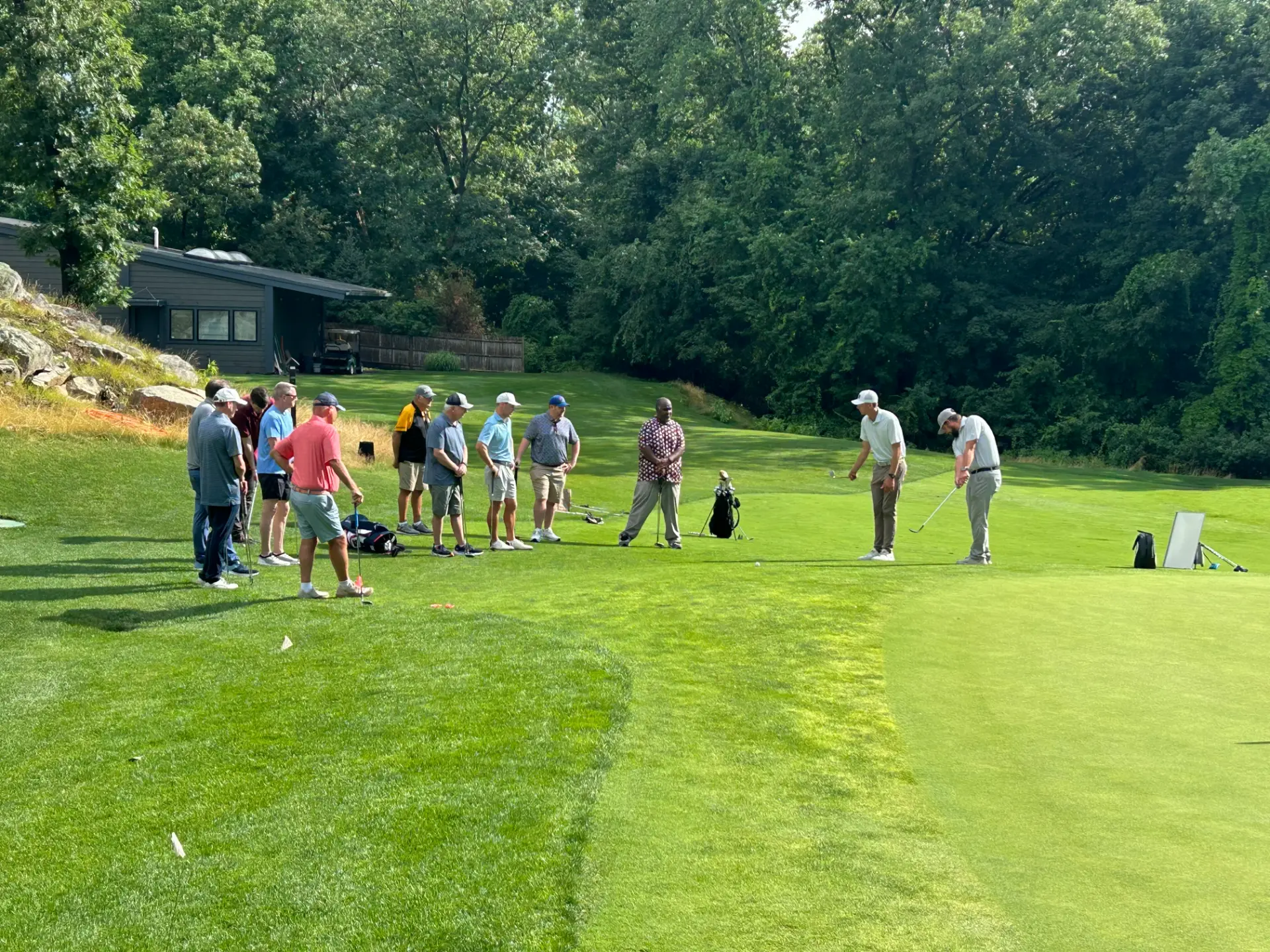 Adult clinic group watching a coach demonstrate on the KOHR practice green